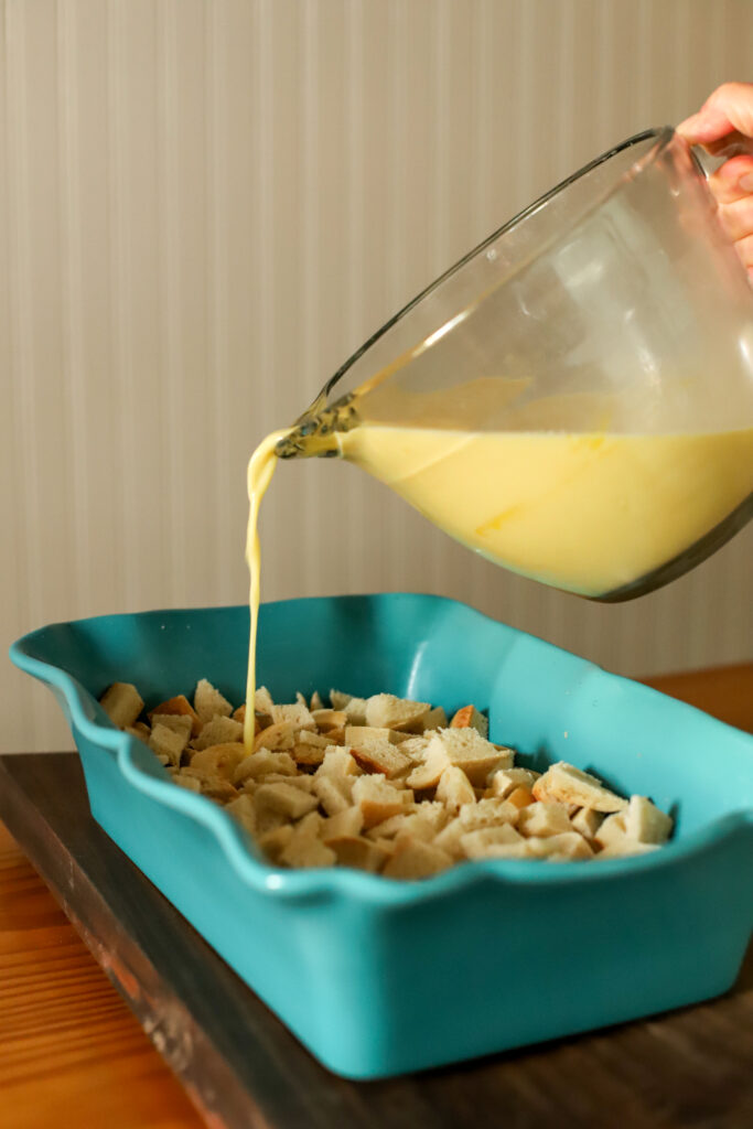 pouring egg and milk mixture over cubed bread