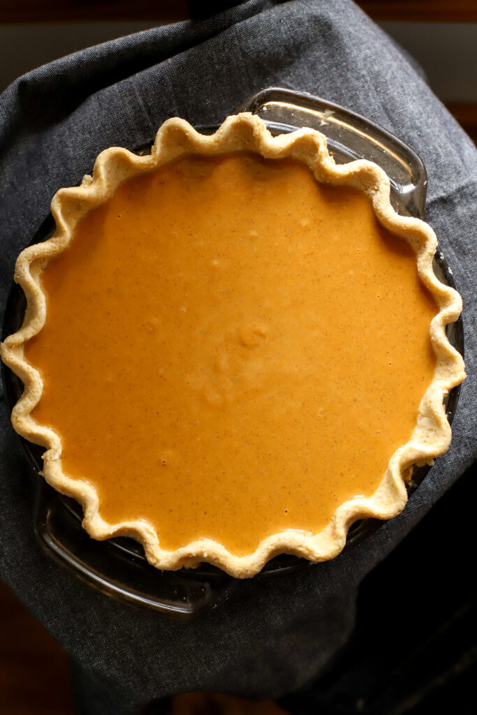 pumpkin pie filling in pan with fluted crust edges