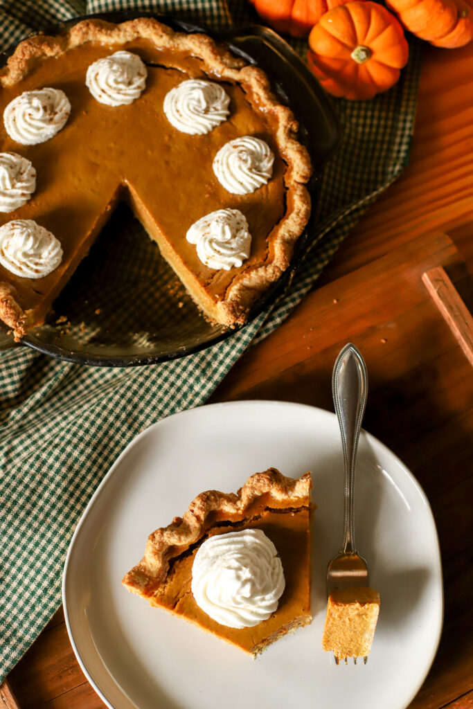 slice of pumpkin pie on a plate with pie in background