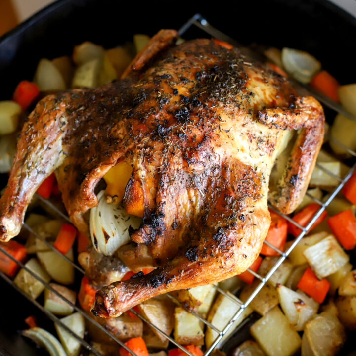 up close shot of whole roasted chicken on top of potatoes carrots and onions
