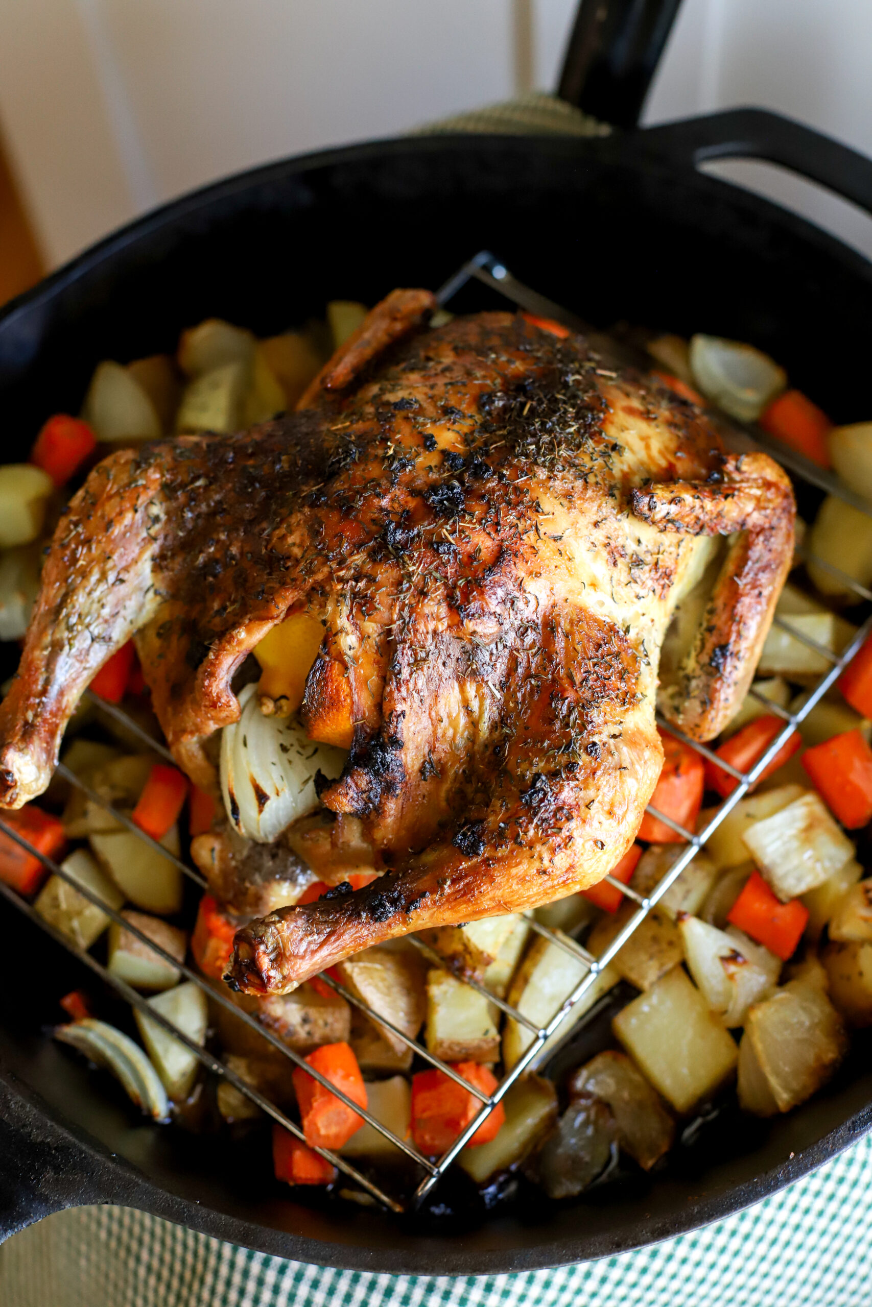 up close shot of whole roasted chicken on top of potatoes carrots and onions