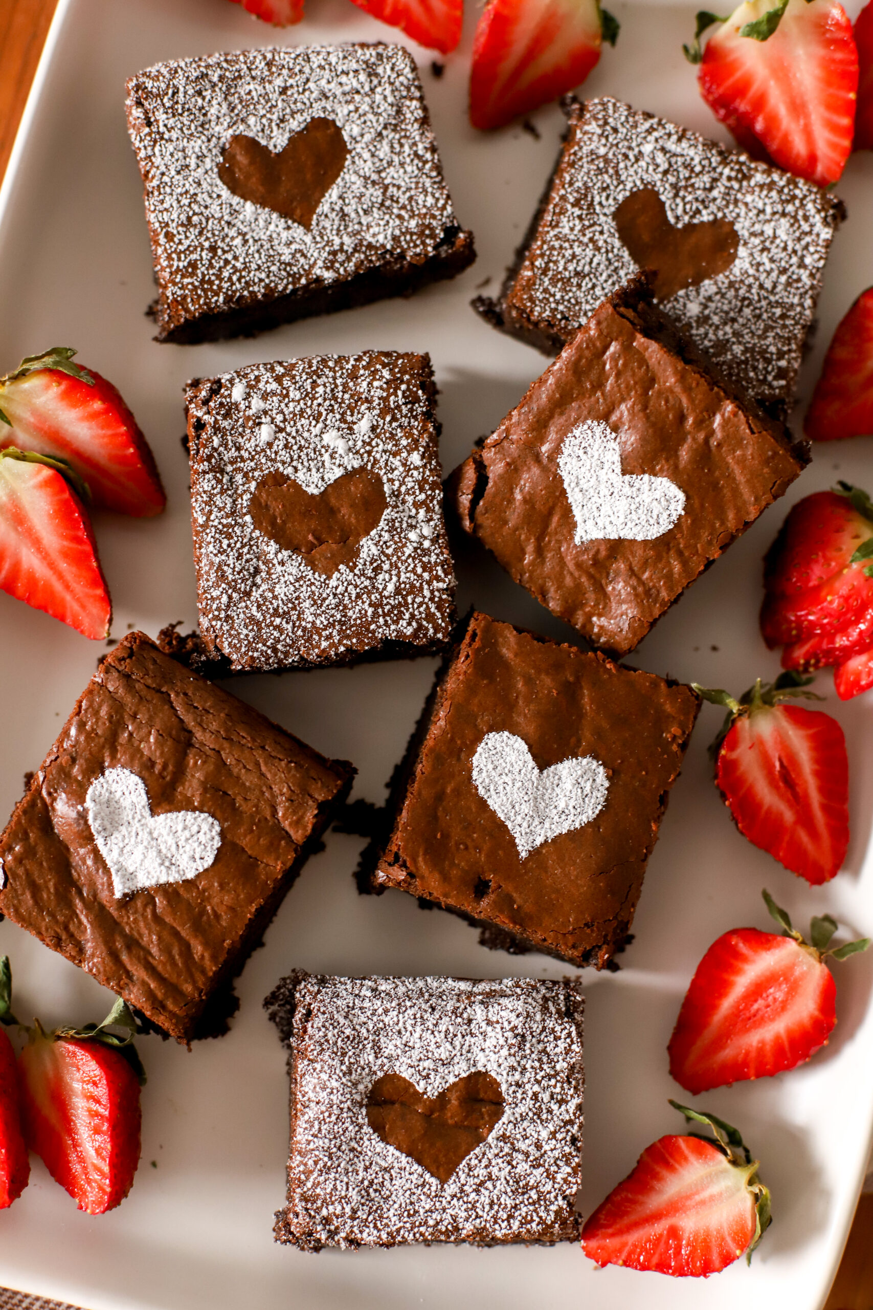 up close shot of fresh milled brownies with powdered sugar on top and sliced strawberries