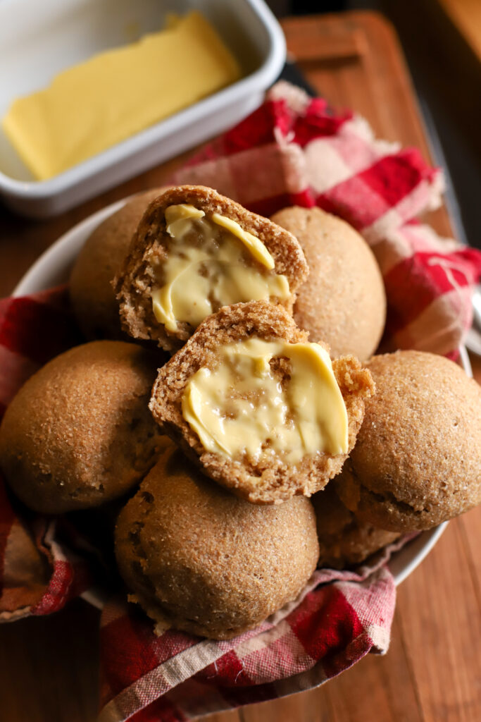 up close shot of buttered fresh milled sourdough dinner rolls sitting on a pile of rolls
