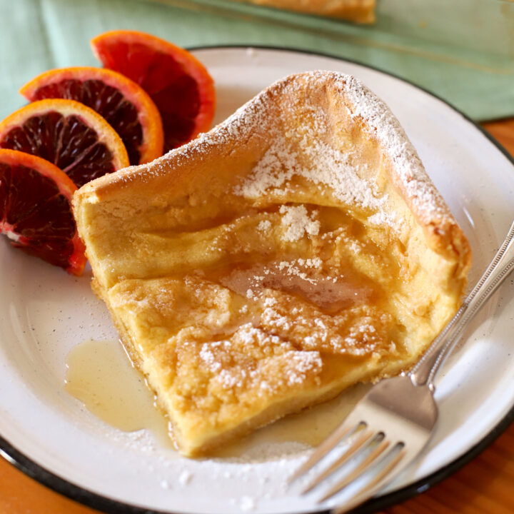 up close shot of slice of fresh milled german pancakes on a plate with slices oranges
