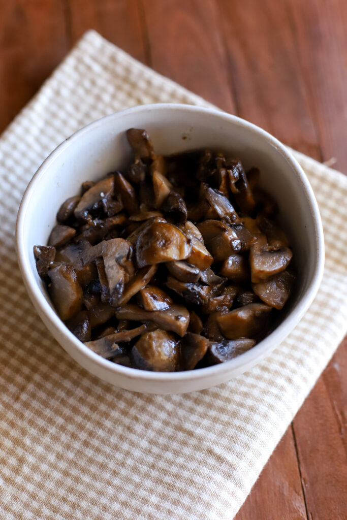 up close shot of a bowl of sauteed mushrooms with a gingham towel underneath