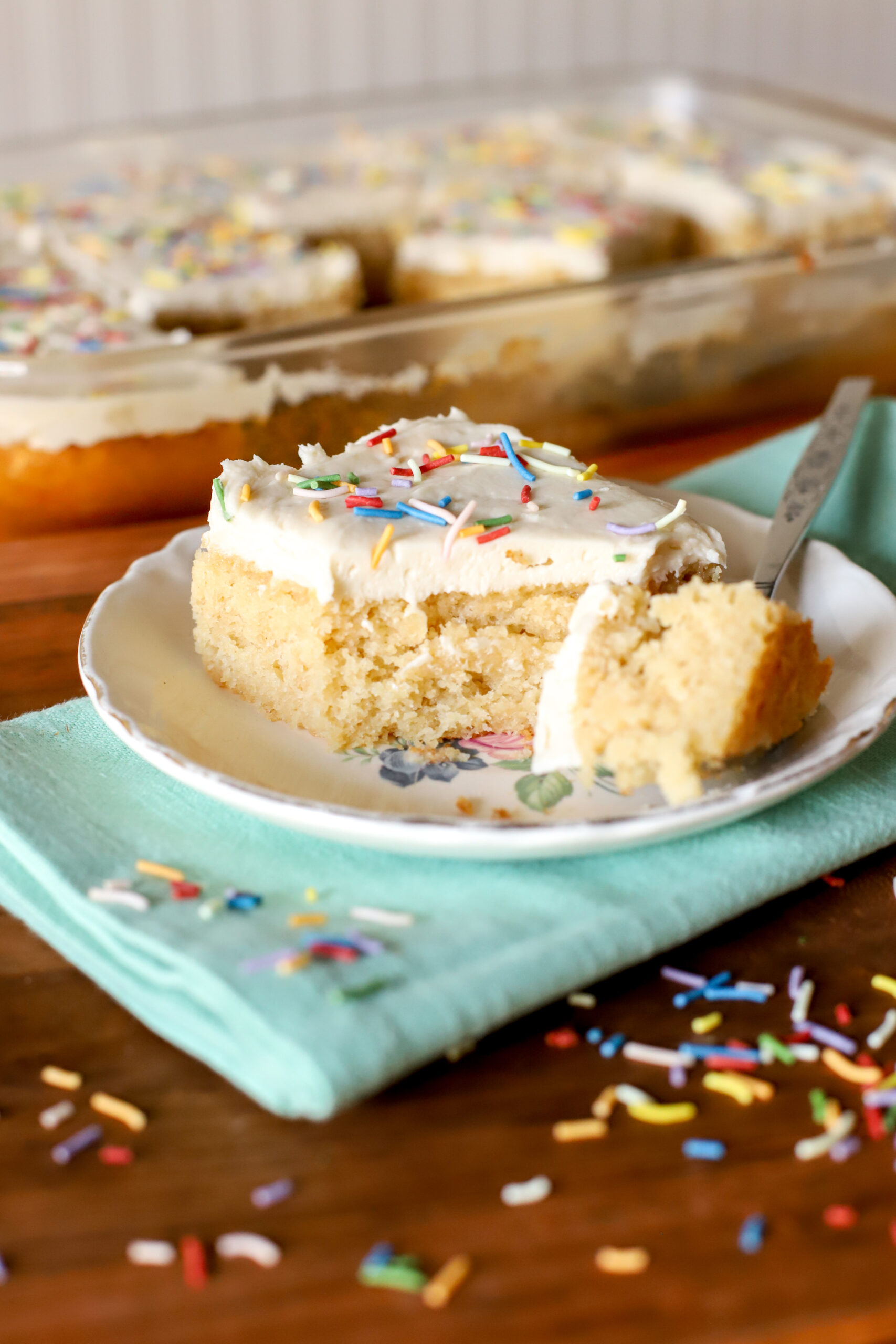 up close shot of a slice fresh milled vanilla cake with a bite taken out on a plate with sprinkles scattered over it