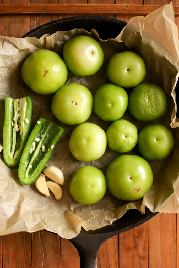 up close shot of a cast iron skillet lined with parchment paper and filled with tomatillos, garlic, and jalapenos