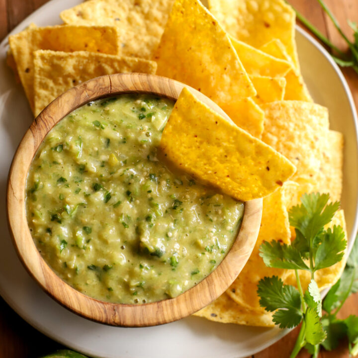 up close shot of bowl of salsa verde surrounded by chips, sliced limes, and cilantro