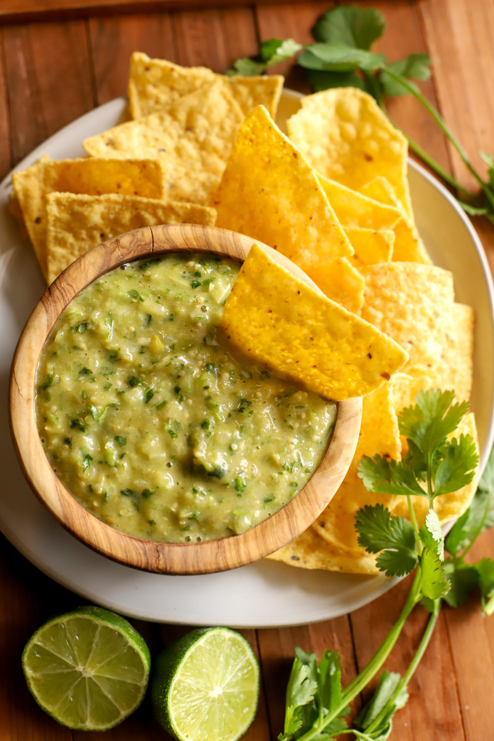 up close shot of bowl of salsa verde surrounded by chips, sliced limes, and cilantro
