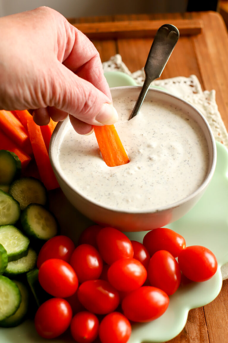 up close shot of a plate filled with vegetables and a bowl of homemade ranch dressing with a carrot dipped into it