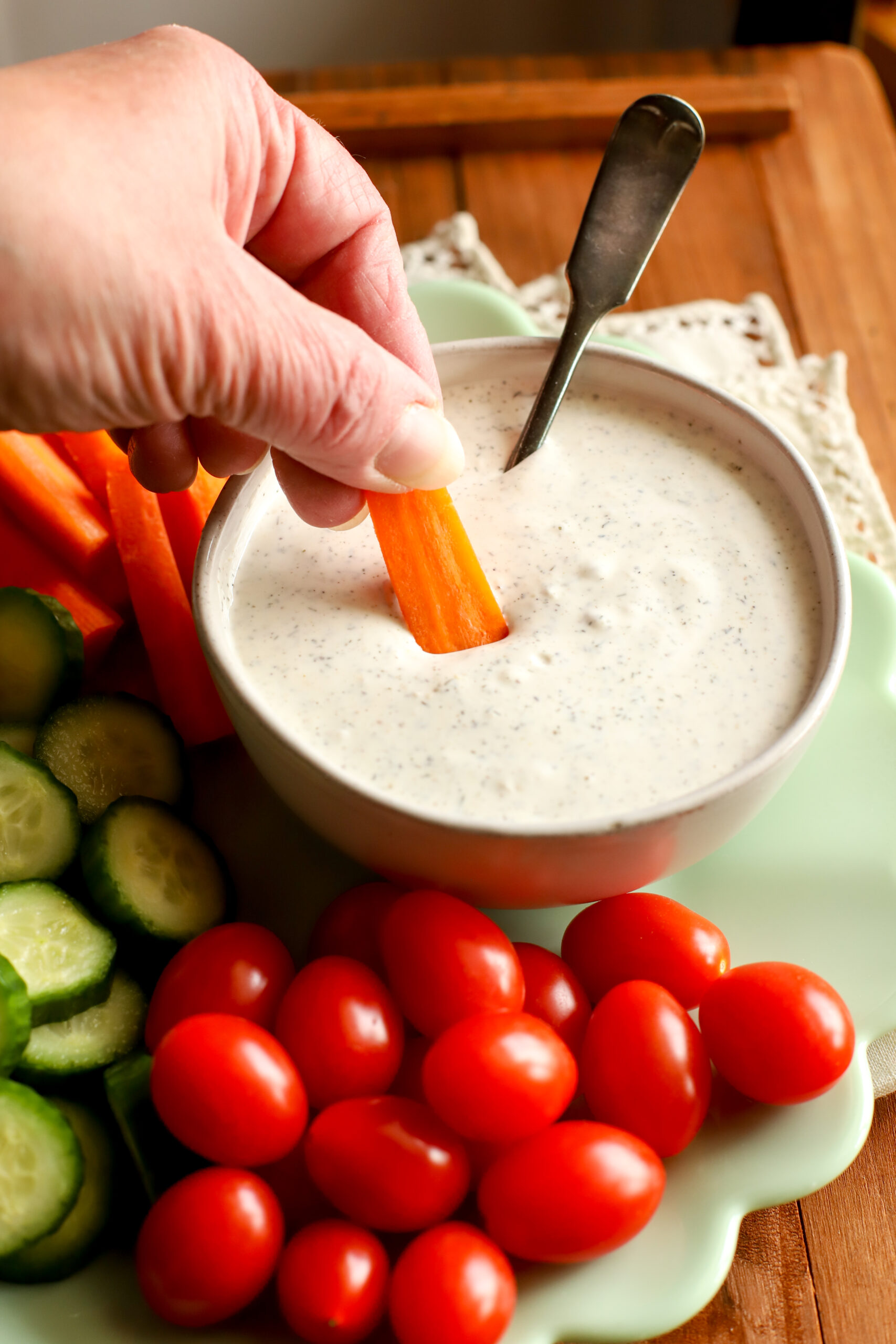 up close shot of a plate filled with vegetables and a bowl of homemade ranch dressing with a carrot dipped into it