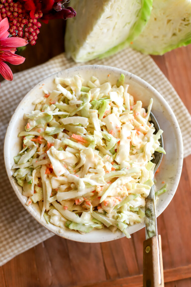 up close shot of creamy coleslaw in a bowl on a wooden table with a white and tan check towel
