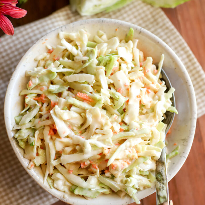 up close shot of creamy coleslaw in a bowl on a wooden table with a white and tan check towel