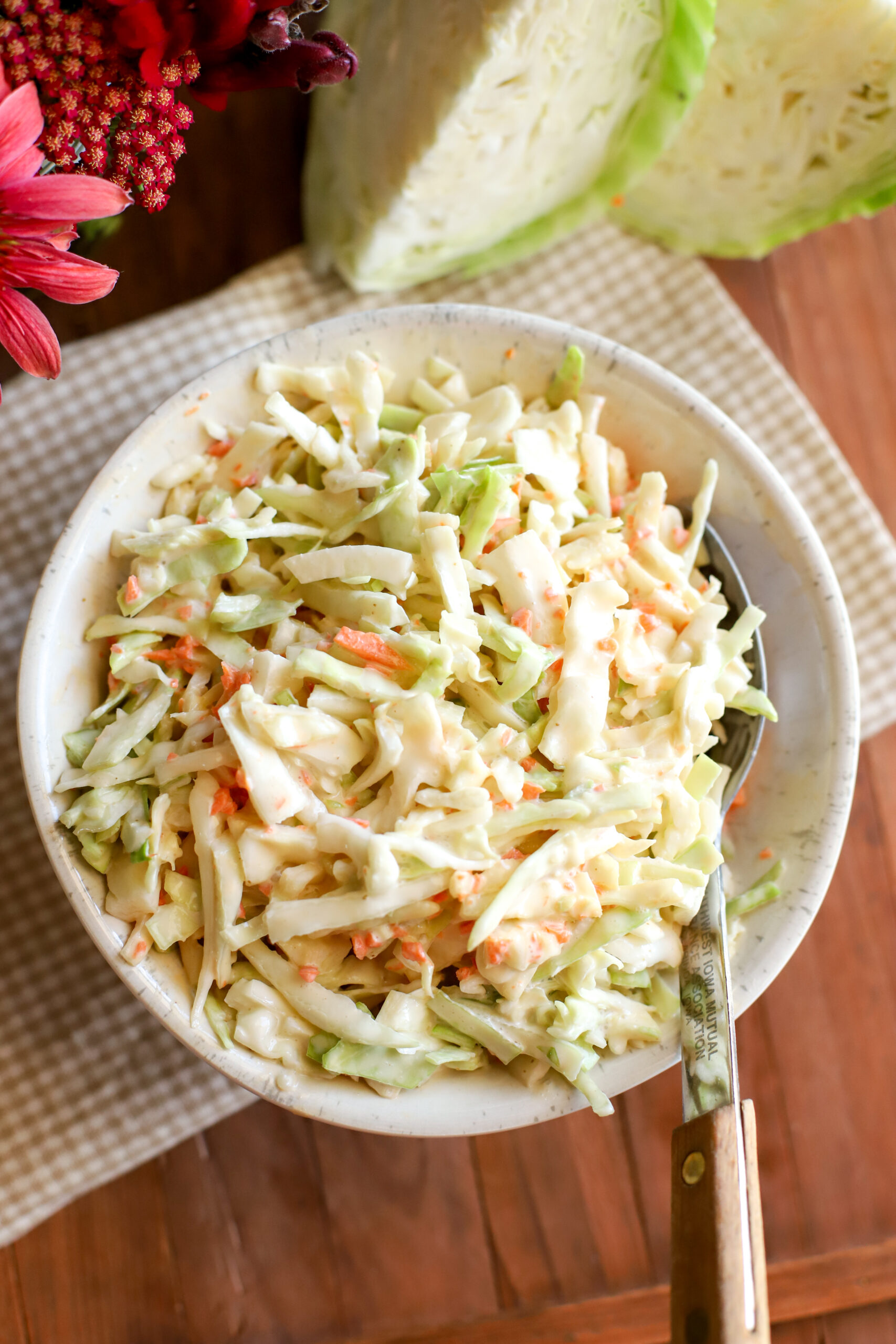 up close shot of creamy coleslaw in a bowl on a wooden table with a white and tan check towel