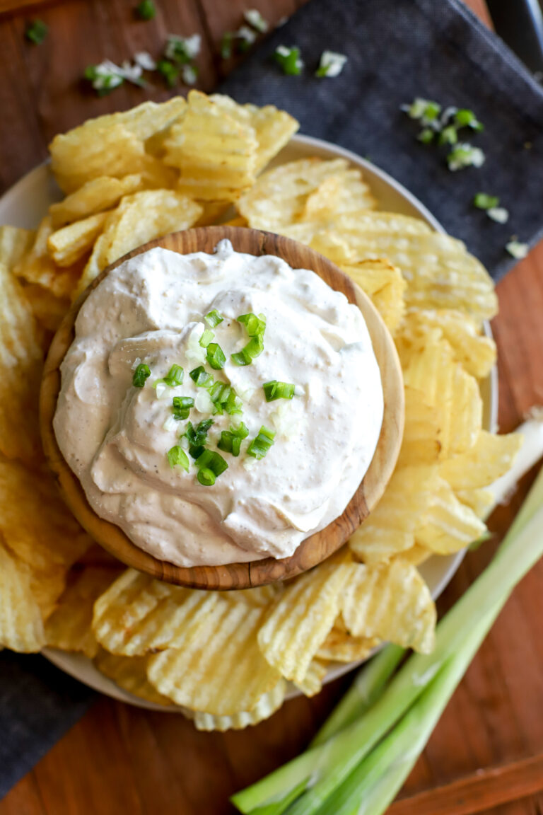an overhead shot of potato chip dip in a bowl with a garnish of green onion surrounded by potato chips
