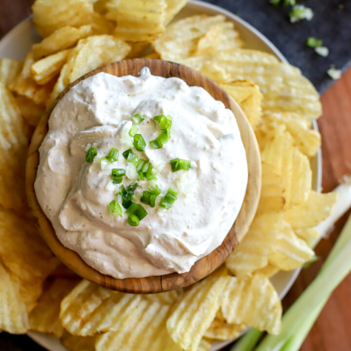 an overhead shot of potato chip dip in a bowl with a garnish of green onion surrounded by potato chips