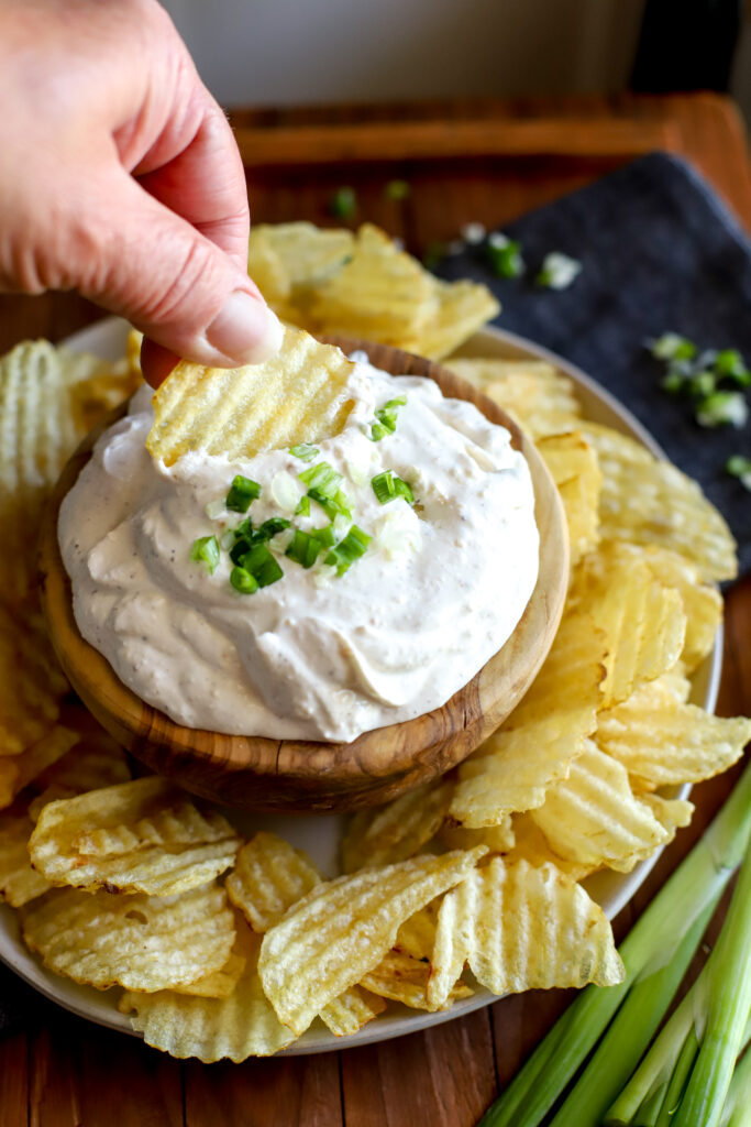 up close shot of a hand dunking a potato chip into a bowl of french onion dip
