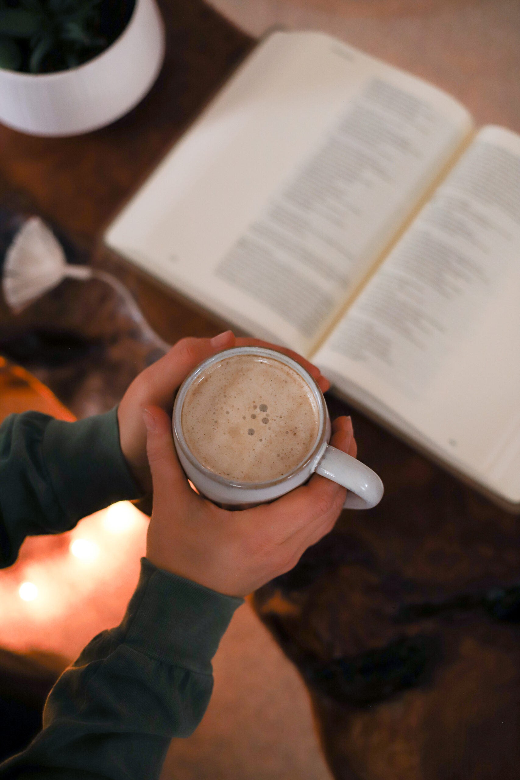 up close shot of hands holding a cup of coffee with bible open in the background
