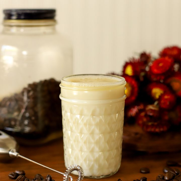 an up close image of homemade caramel coffee creamer in a jar surrounded by coffee beans