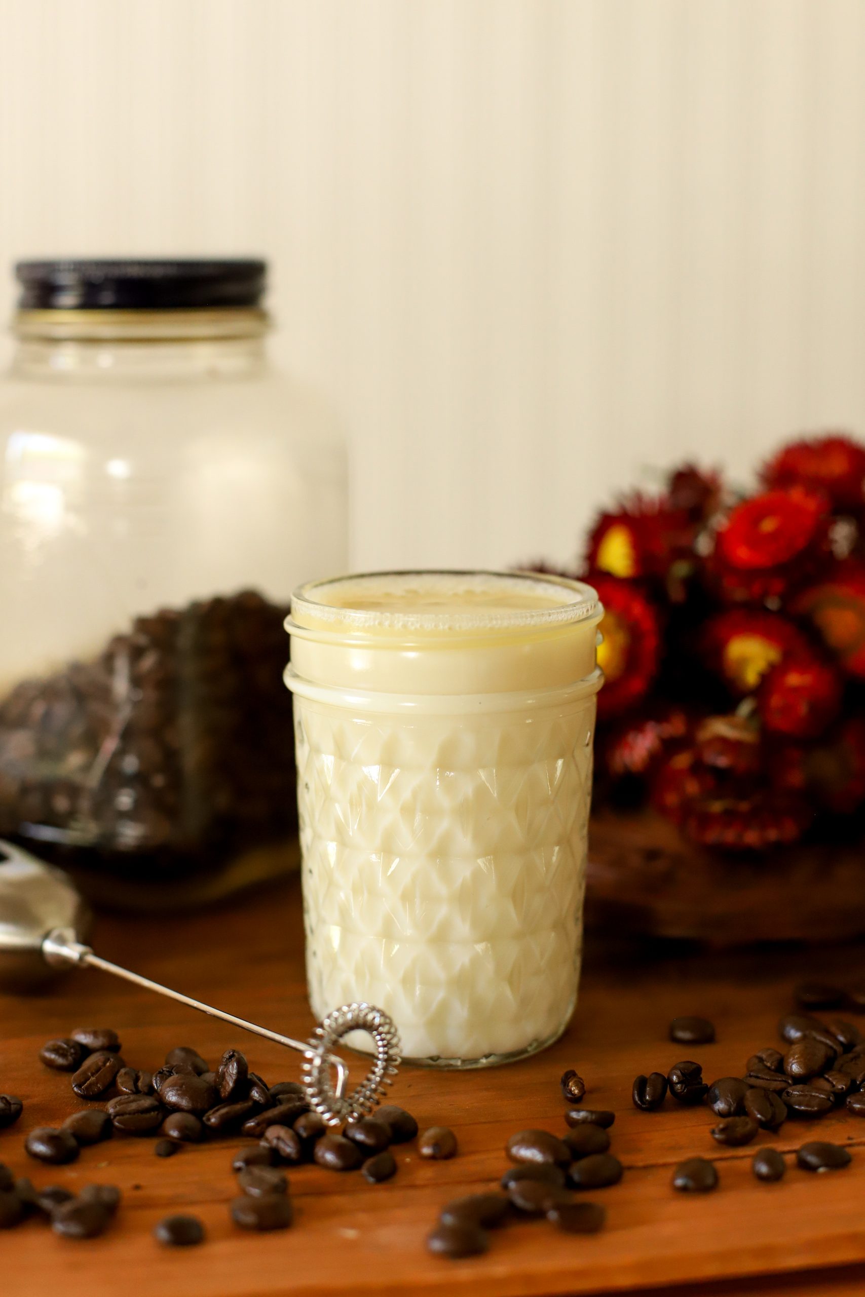 an up close image of homemade caramel coffee creamer in a jar surrounded by coffee beans