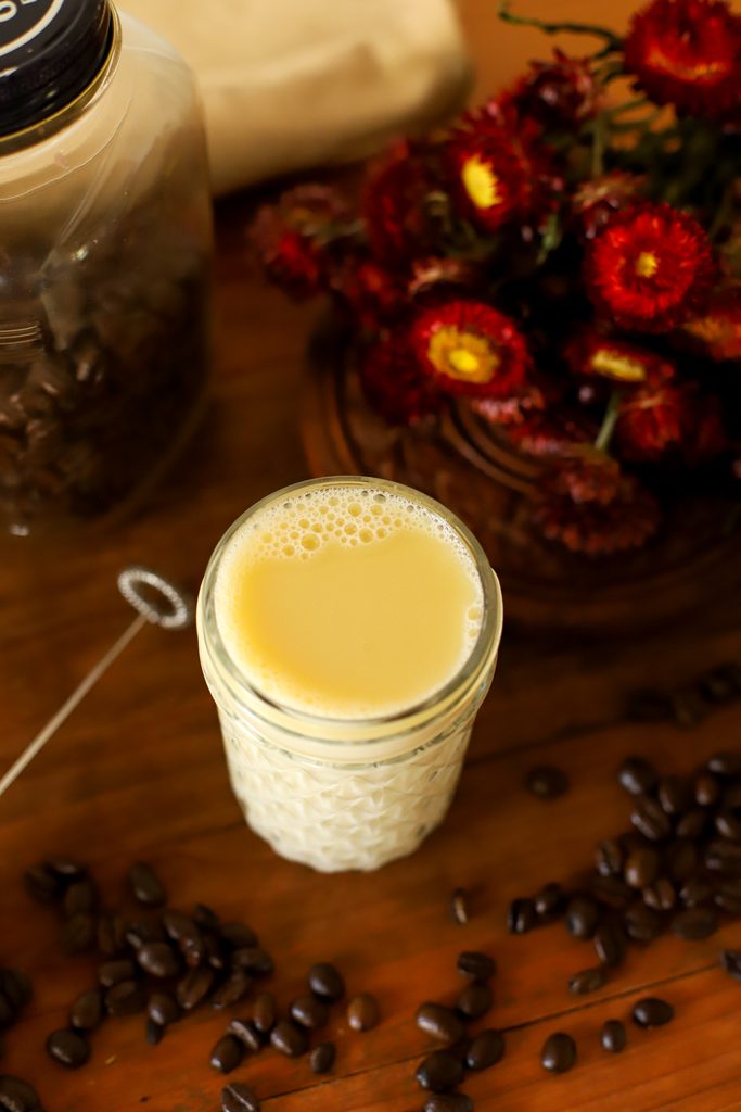 an up close image of homemade caramel coffee creamer in a jar surrounded by coffee beans