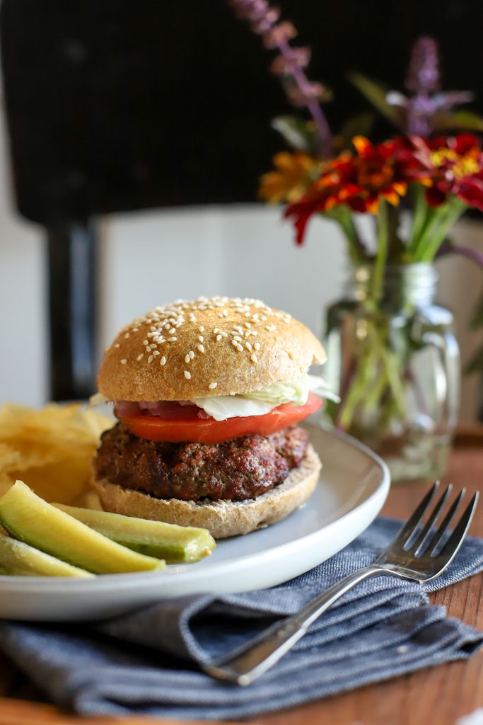an up close shot of a hamburger with a fresh milled burger bun on a plate with pickles and chips