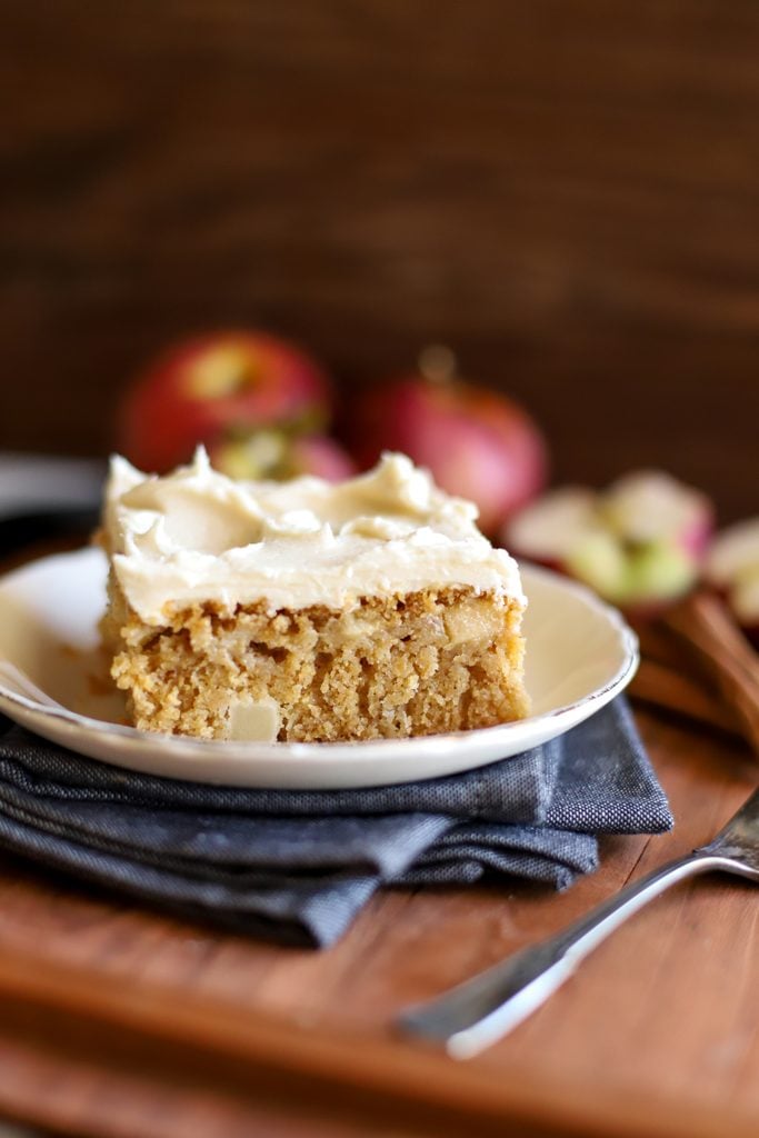 an up close shot of a slice of fresh milled flour apple cake on a plate with apples in the background