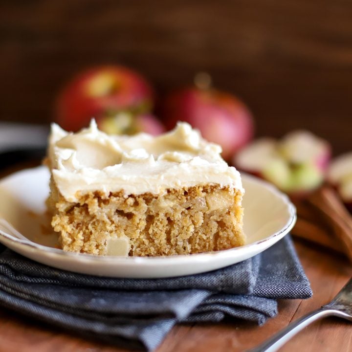 an up close shot of a slice of fresh milled flour apple cake on a plate with apples in the background